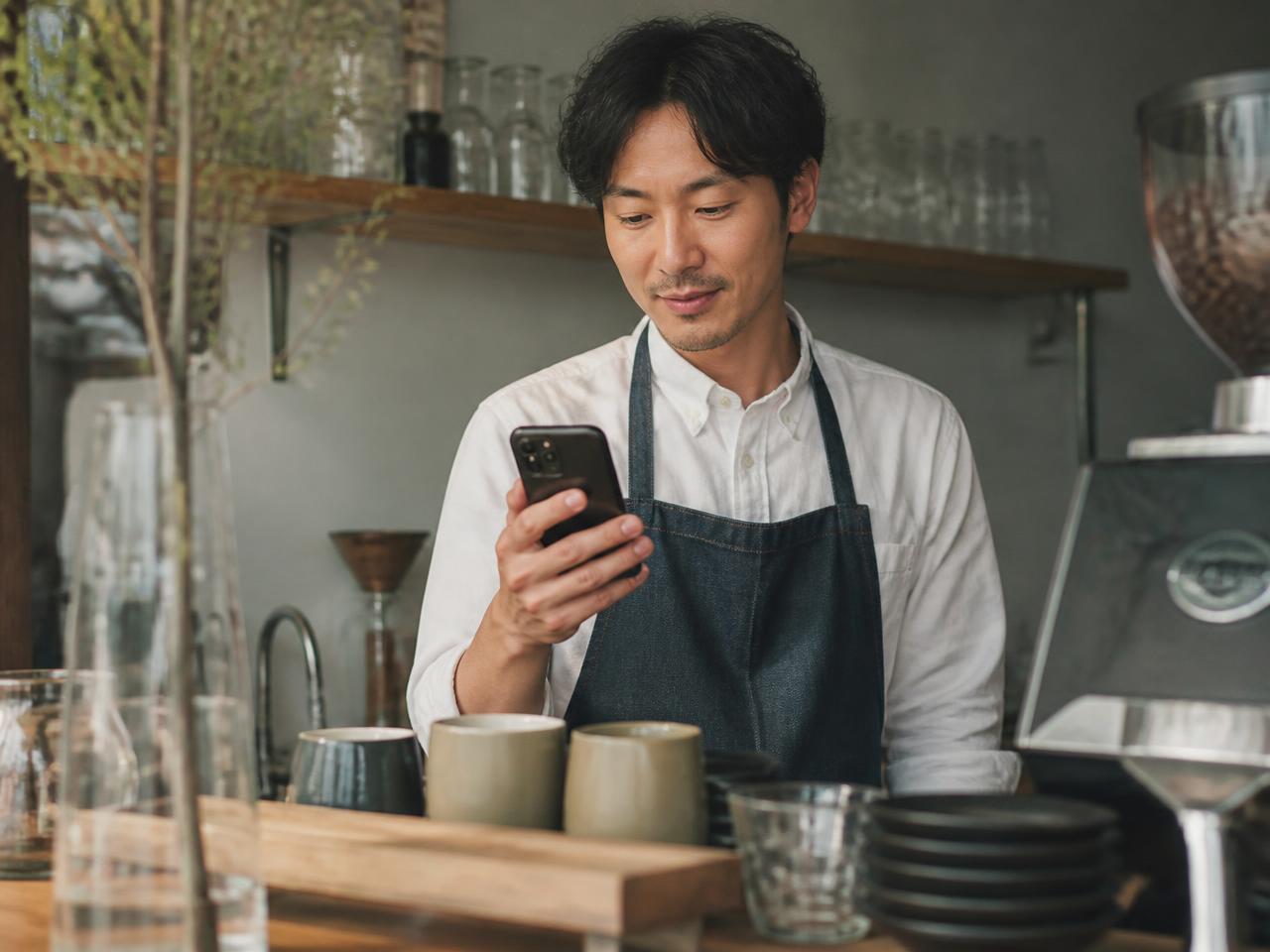 Café owner replying to a customer message from his phone behind the counter.
